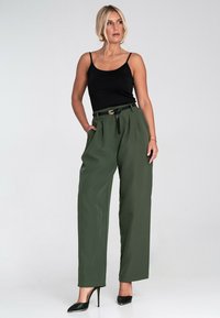 Oliwkowe szerokie spodnie z wysokim stanem, plisami i czarnym paskiem z złotą klamrą. Połączone z czarnym topem na ramiączkach i wysokich obcasach.