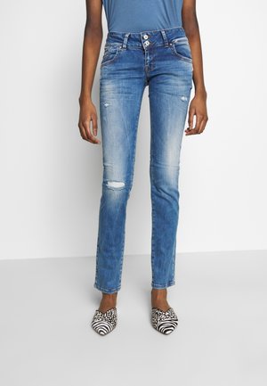 Jeans de mezclilla azul con un corte recto, que presentan detalles desgastados y un lavado claro. Acompañados de zapatos con un patrón en blanco y negro.