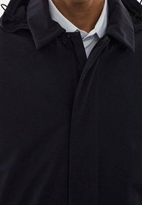 Chaqueta negra con cuello alto y cierre de cremallera, presenta una textura suave y detalles mínimos. Corte entallado alrededor de los hombros.