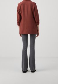 Rust-colored blazer with rolled sleeves, long back, paired with gray flared jeans. Smooth fabric with a simple design.