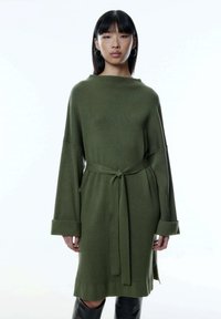 Langärmliges, olivgrünes Strickkleid mit einem lockeren Schnitt, weiten Bündchen und einem Bindegürtel in der Taille. Strukturierter Rippenmuster über das gesamte Kleid.