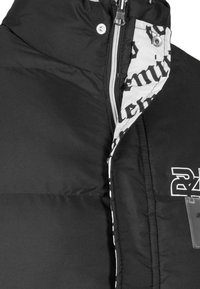 Jachetă neagră puffer cu guler înalt, fermoar argintiu și un căptușeală interioară cu un model de text îndrăzneț, evidențiind textura stratificată a materialului.