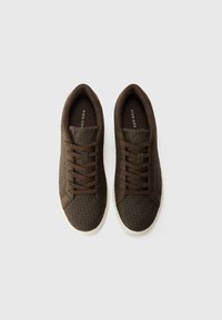 Zapatillas marrones con una textura trenzada, punta redondeada y cordones marrones a juego. Suela de goma blanca para contraste y diseño ligero.
