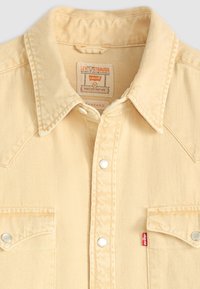 Beige Levi's denimskjorte med spiss krage, metall trykknapper, klaftelommer på brystet, og synlig Levi's-merke på brystlomma og krageetikett.