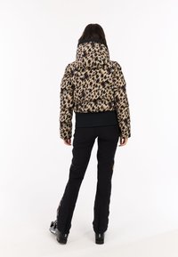 Geknipt pufferjack in een leoprint stof, met een hoge kraag en zwarte elastische zoom. Zwarte broeken met zijritsen maken de look compleet.