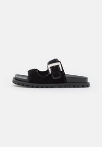 Black slide sandal with thick lug sole, suede straps, and a large square silver buckle on the upper strap against a white background.