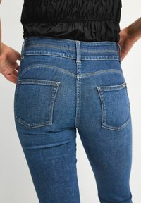 Blå denimjeans med en figursydd design, som har två bakfickor och diskret sömnad. Tyget har en mjuk textur och en lätt blekning.