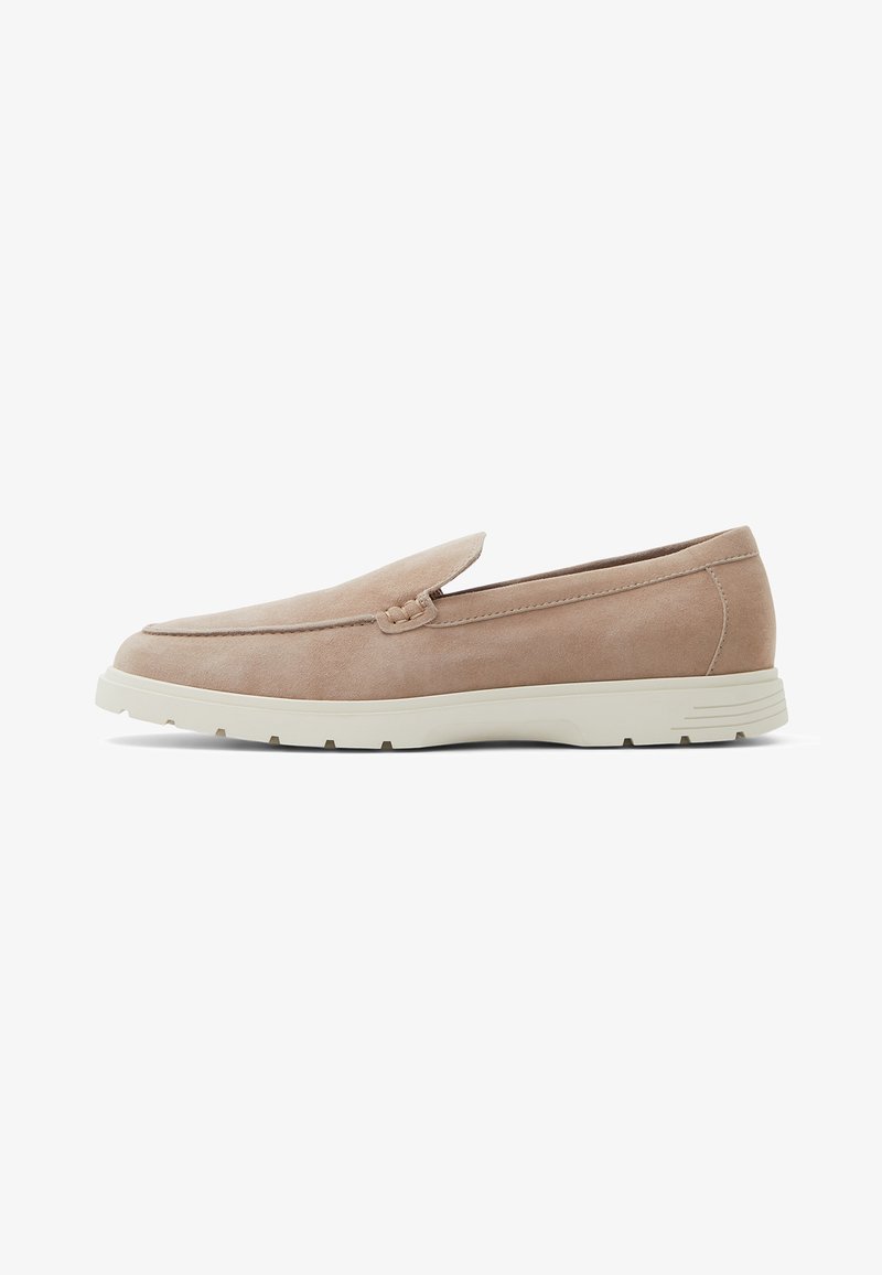 Beige ruskindsloafers med en rund tå, diskret syedetaljer og en hvid gummisål, med en flad hæl og slip-on design.