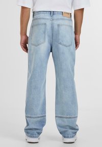 Svetlo modri jeans z ohlapnim krojem, ki vključujejo dva zadnja žepa, blagovno znamko iz usnja in širok kroj nog.