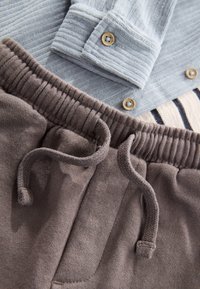 Graues gestreiftes Hemd mit Knöpfen, über braunen Sweatpants mit elastischem Bund und Kordelzug, glatter Textur und Seitentaschen.
