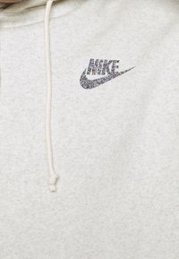 Ljusgrå huvtröja i mjukt tyg med en glittrande svart Nike-logotyp på bröstet och huva med dragsko.