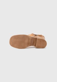 Bota de cuero marrón claro con un acabado suave, con la punta redondeada y una suela robusta y con bandoleras. Con un hebilla decorativa en el lateral.