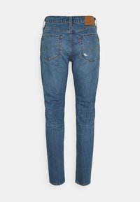 Vue arrière d'un jean en denim bleu coupe slim, deux poches arrière, usure subtile et patch en cuir marron sur la ceinture.