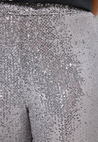 Pantaloni argentati con paillettes con superficie testurizzata, dotati di una vestibilità aderente e una cintura elastica, che riflettono la luce con un effetto luccicante.