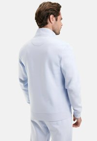 Sweatshirt bleu clair avec un col montant, des poignets et une taille côtelés. Tissu doux avec une texture lisse et un design minimaliste.