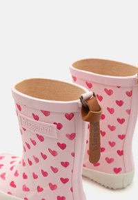 Bottes de pluie en caoutchouc roses avec un motif en forme de cœur dans des nuances variées de rose, doublées d'un intérieur beige et dotées d'une languette en cuir marron.