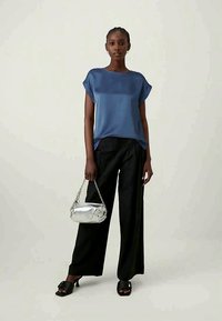 Blusa blu fluida con maniche corte, abbinata a pantaloni neri a gamba larga e sandali neri con zeppa. Accessoriata con una borsa argentata.