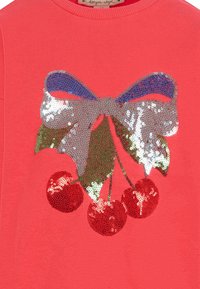 Koraal sweatshirts met een sequins kersontwerp, een zilveren en blauwe band, groene bladeren en glanzende rode kersen. Zachte stoftextuur.