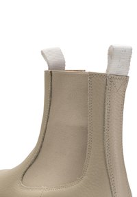 Bota de tobillo de cuero beige con paneles laterales elásticos, superficie texturizada y una lengüeta en la parte posterior para facilitar su uso. Acabado suave, diseño minimalista.