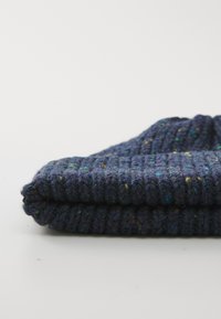 Folded dark blue knitted sweater with multicolored specks placed on a plain white surface.
