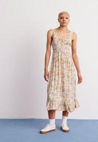 Maxi-jurk met bloemenprint van lichtgewicht stof, met een smock-buste, dunne bandjes en een gerimpelde zoom. Ggedragen met witte schoenen en enkelsokken.