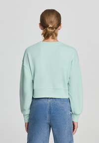 Felpa corta verde menta con maniche lunghe, polsini a costine e scollatura rotonda, abbinata a jeans in denim blu a vita alta.