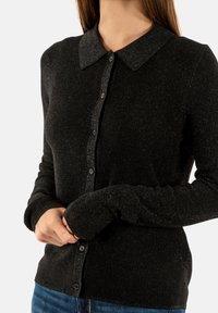 Cardigan nero dal tessuto texturizzato con colletto, apertura con bottoni e polsini a costine, arricchito da sottili fili metallici per un tocco di dettaglio in più.