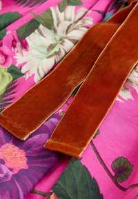 Brune velourstofstrimler ligger på levende pink blomsterstof med store grønne blade og farverige blomster.