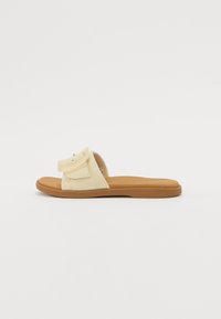 Gule stoffsklisandaler med en enkel justerbar stropp, polstret såle og en brun gummiyttersåle, med et minimalistisk design og søm.