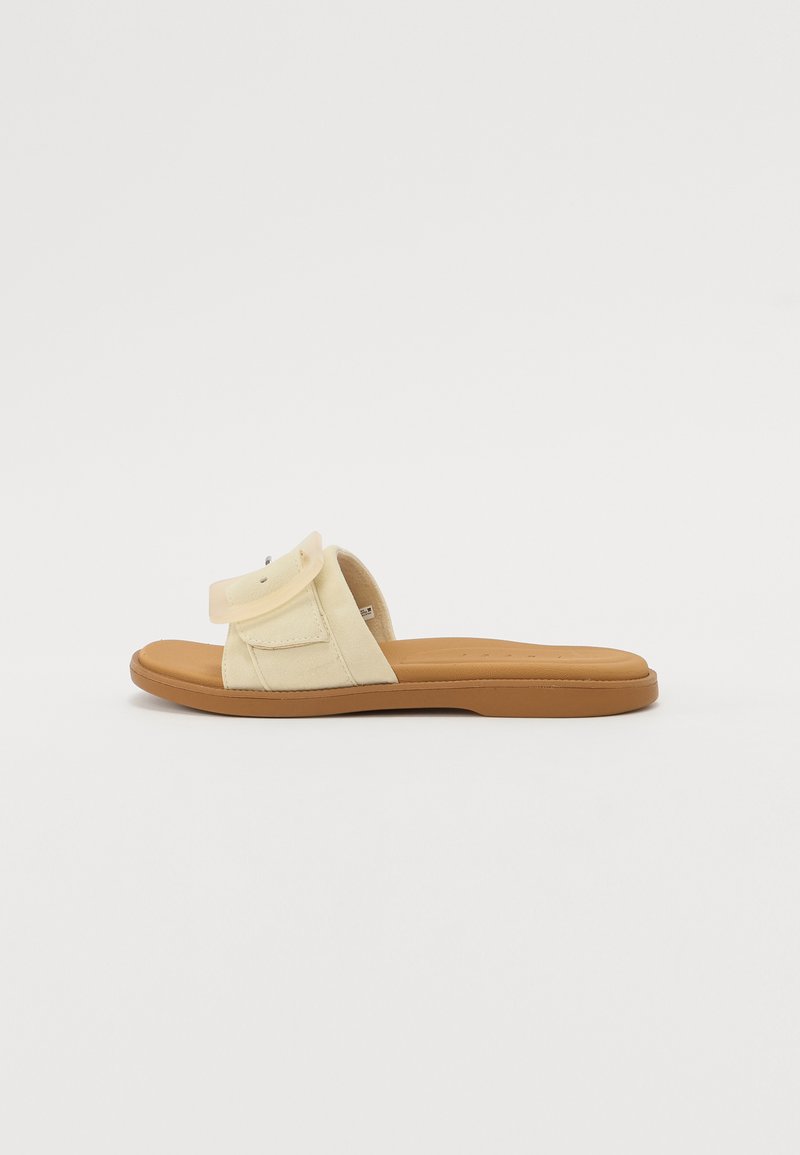 Gule stoffsklisandaler med en enkel justerbar stropp, polstret såle og en brun gummiyttersåle, med et minimalistisk design og søm.