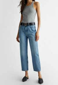 Grå linne, hög midja ljusblå jeans, svart bälte med en cirkulär spänne och svarta texturerade skor utan häl med en dekorativ design.