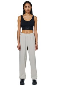 Woman with long braided hair wearing a black crop top and loose light gray trousers with black sneakers, standing facing forward.