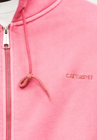 Lyserød hættetrøje med lynlås og snore samt lille broderet "carhartt"-logo på brystet.