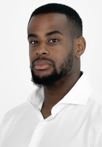 Man met kort zwart haar en een volle baard, die een witte overhemd met kraag draagt. Het overhemd heeft een gladde textuur en een knoopsluiting bij de hals.