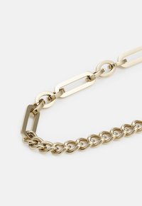 Collier en chaîne dorée avec des maillons ovales et ronds, finition texturée et design massif. Surfaces lisses et brillantes.