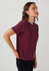 Korte mouwen, ronde hals t-shirt in diep bordeaux. Gemaakt van zacht materiaal met een gladde textuur, aansluitende pasvorm en zonder zichtbare patronen of accenten.