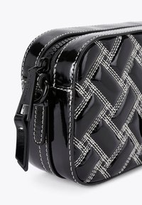 Zwarte lakkatoenen handtas met een gequilt patroon en witte stikselaccenten. Voorzien van een dubbele rits en een stevige draagband.