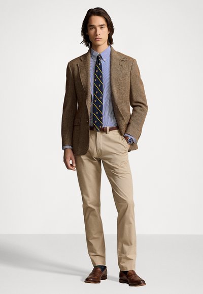 Blazer marrón en espiga sobre una camisa a rayas azul clara, complementado con una corbata azul marino con acentos dorados, pantalones beiges y mocasines marrones.