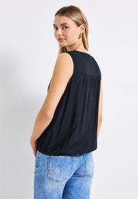 Top nero senza maniche con retro plissettato e bordo elastico, abbinato a jeans in denim blu chiaro, che mostrano una vestibilità comoda.