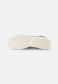 Semelle de chaussure en caoutchouc blanche avec un motif de bande de roulement en zigzag, featuring un logo en relief et une texture lisse. Accents noirs sur les côtés.