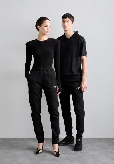 Svart långärmad topp med axelsömmar, kombinerad med svarta joggers med elastisk midja. Manlig modell i svart polo och joggers.