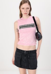 Rosa, kort, ermeløs topp med en teksturert sort akzent og glidelåsdetalj. Kombinert med en svart denim miniskjørt med lommer.