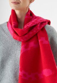 Roter Schal mit pinken Mustern, aus weichem, strukturiertem Stoff, um den Hals drapiert, kombiniert mit einem hellgrauen Pullover.