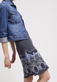 Giubbotto di denim con un taglio classico e lavaggio chiaro, abbinato a un vestito lungo fino al ginocchio che presenta un design a motivo blu e nero.