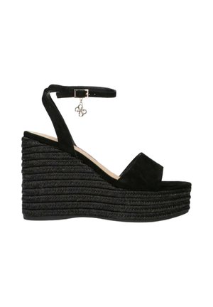 Sandalo zeppa nero con suola piatta intrecciata, cinturino alla caviglia con fibbia e piccolo dettaglio di ciondolo pendente.