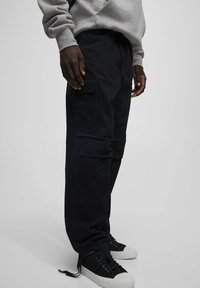 Czarne spodnie cargo wykonane z bawełny, z bocznymi kieszeniami, luźnym krojem i regulowanymi mankietami. W połączeniu z czarnymi trampkami i szarym swetrem.
