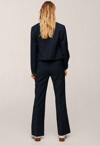 Navy suit with a cropped blazer and flared pants, made of textured fabric. Features a clean back seam and simple button accents.