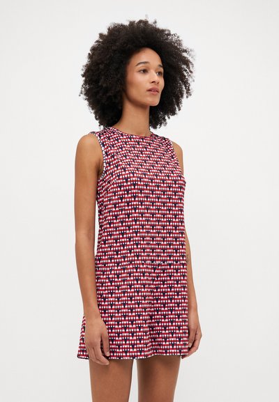 Beigalė suknelė, išsiskirianti raudonai baltu geometriniu raštu, pagaminta iš minkštos medžiagos, su laisvu siluetu ir apvaliu iškirpimu.