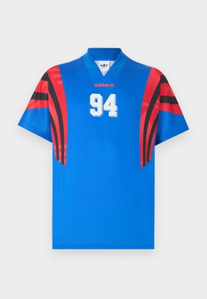 Camiseta deportiva azul de Adidas con patrones geométricos rojos y negros en las mangas, número blanco 94 centrado debajo del pequeño logo rojo de Adidas.