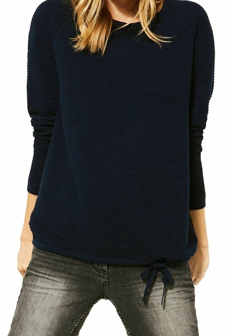 Mörkblå texturerad sweatshirt med långa ärmar, rund halsringning och dragsko i nederkant, tillsammans med grå jeans.